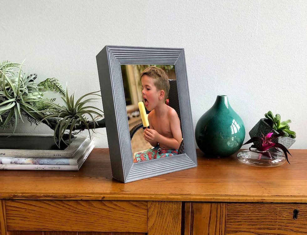 A great picture frame on a wood table with a child eating a popsicle on the screen