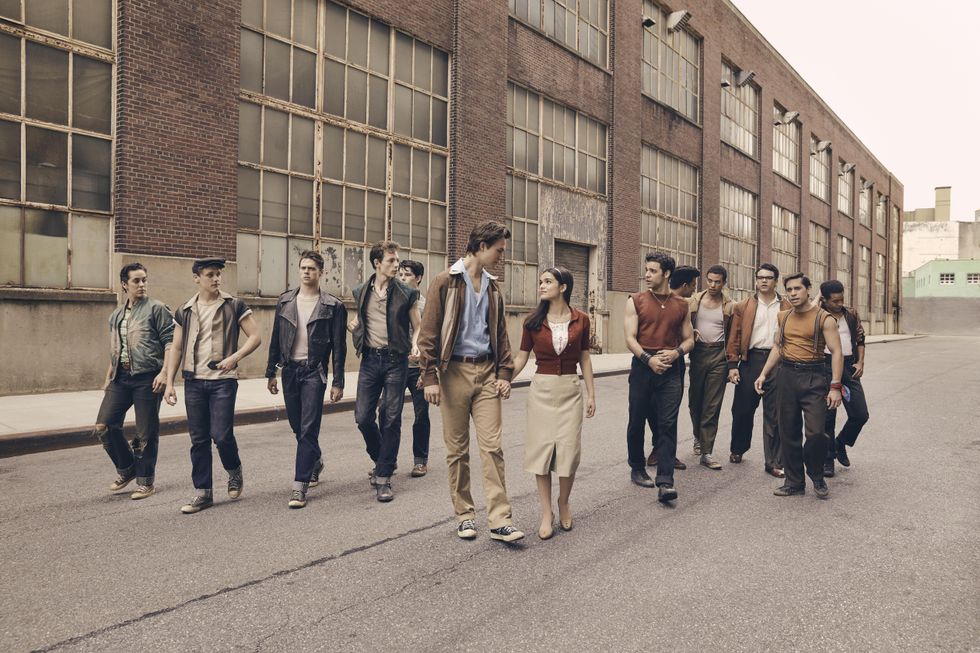 A group photo of the ensemble Jetts and ensemble Sharks following Ansel Elgort as Tony and Rachel Zegler as Maria in a promotional still for "West Side Story."