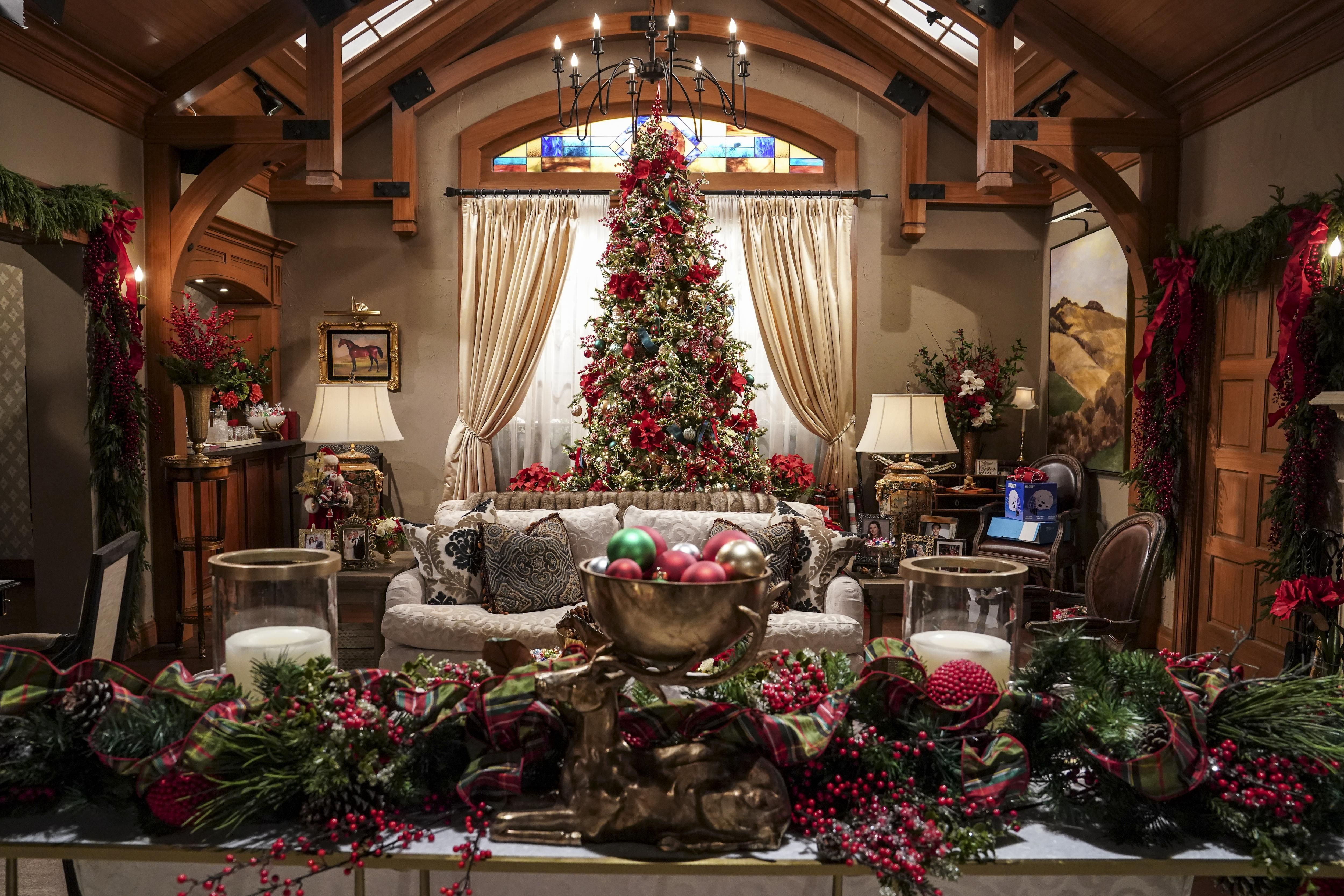 A large indoor Christmas tree is in the background of a living room while garland covered furniture is in the foreground