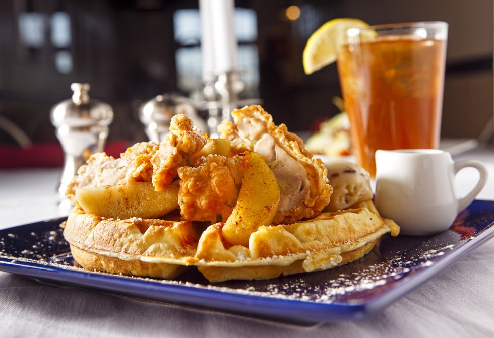 Fried chicken and peaches stacked on a waffle with syrup on the side. A glass of sweet tea is in the background.