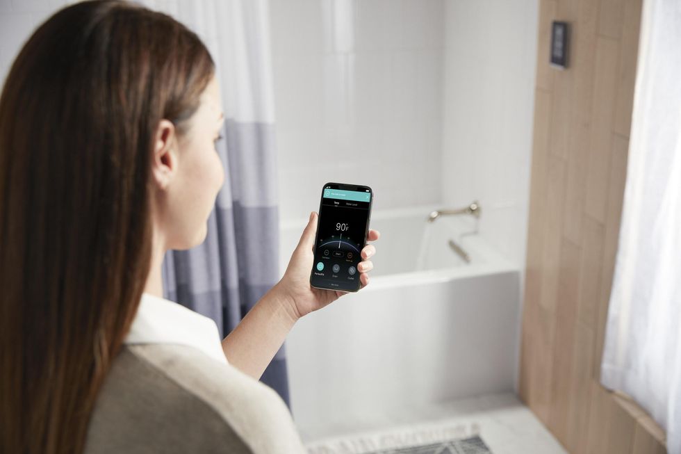 Kohler PerfectFill Bath Filler and Drain on a tub with a woman controlling it via a smartphone app