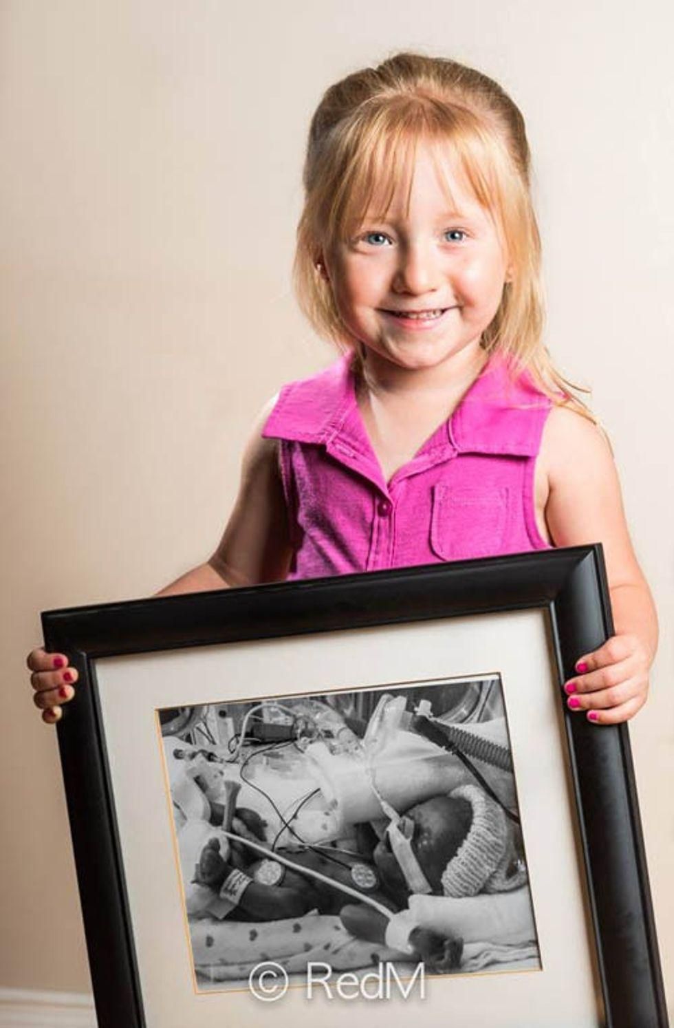 a little girl holds a black and white photograph of herself as a premature baby