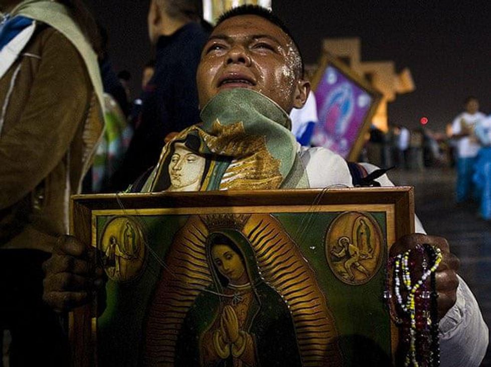 A man is on his knees crying with a frame with La Virgen de Guadalupe and Rosarios in his hands.