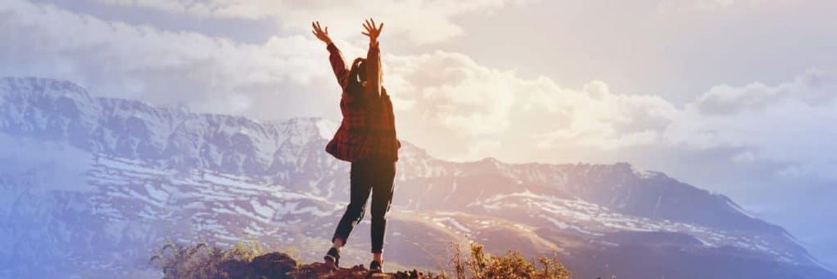 woman standing arms-stretched at the top of a mountain overlooking the mountain scenery