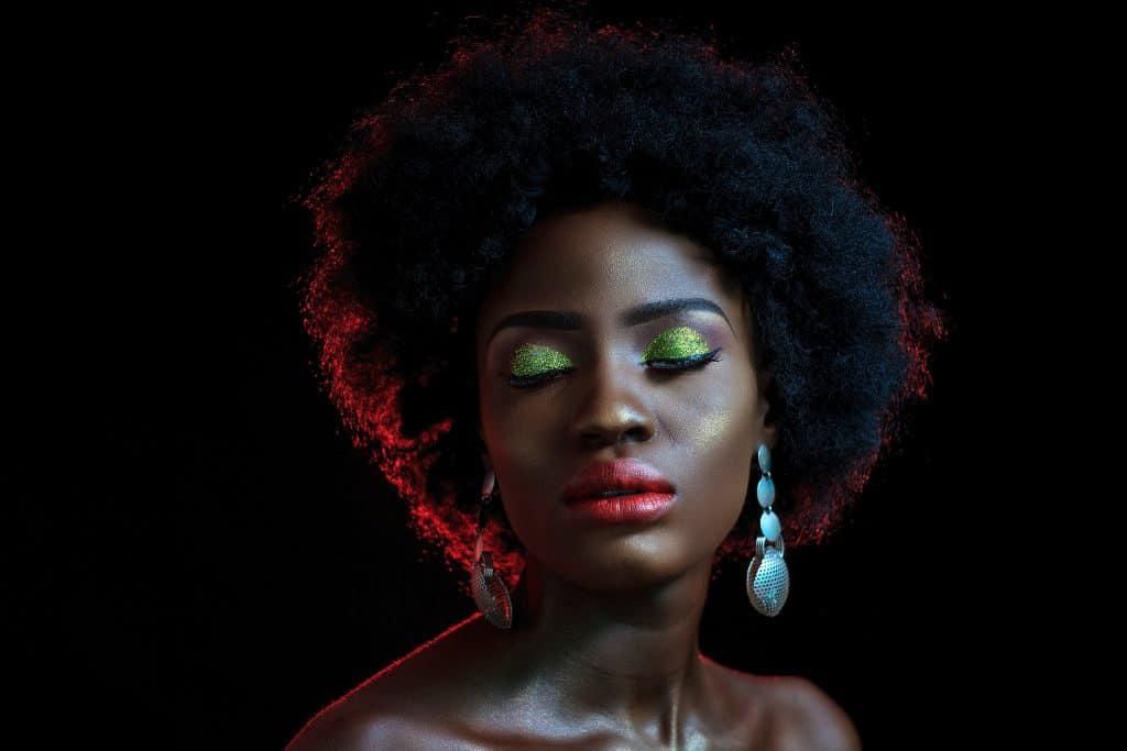beautiful dark-skinned woman with big hair, colorful makeup, and a dangling blue earring