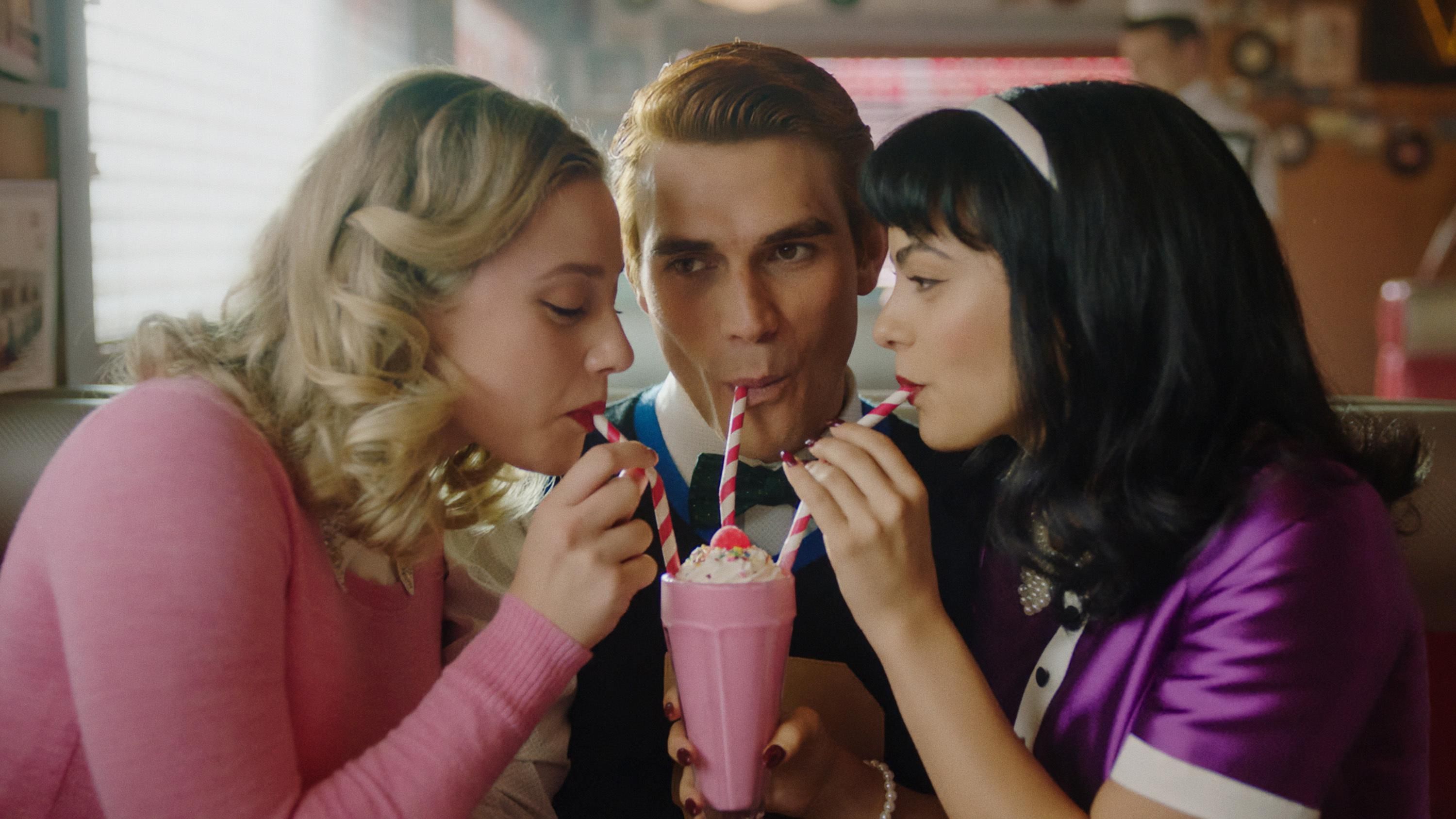 Archie shares a strawberry milkshake with Betty and Veronica in a booth at Pop's