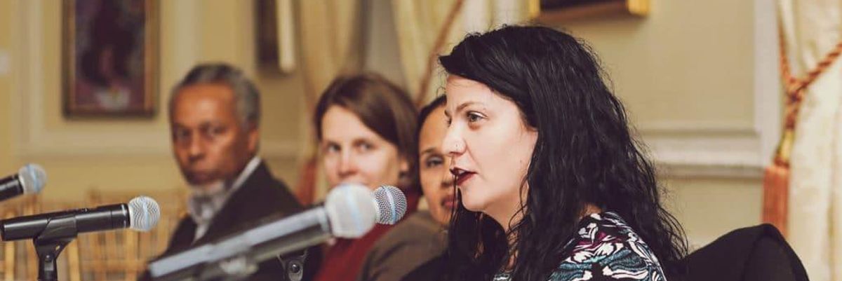 woman, Jessica Krug, speaking to a microphone with two women and a man behind her
