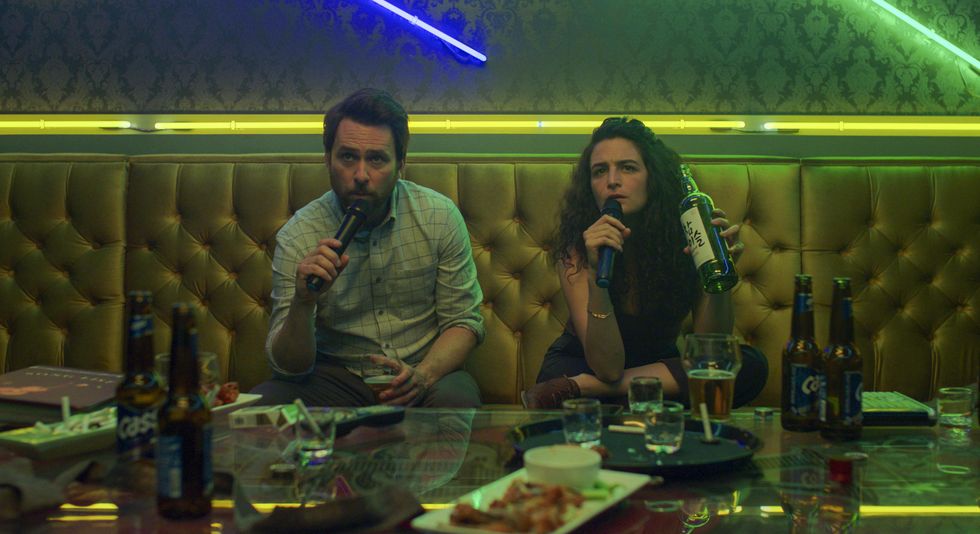 An image of ​Charlie Day (left) and Jenny Slate (right) in Amazon Prime's newest rom-com film "I Want You Back." They're singing in a karaoke bar with lots of alcohol and food in the foreground.