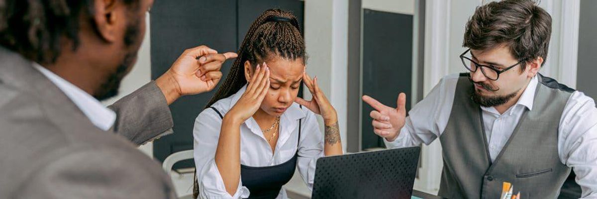 woman with overwhelmed expression sitting at a computer with a man on each side of her pointing at her