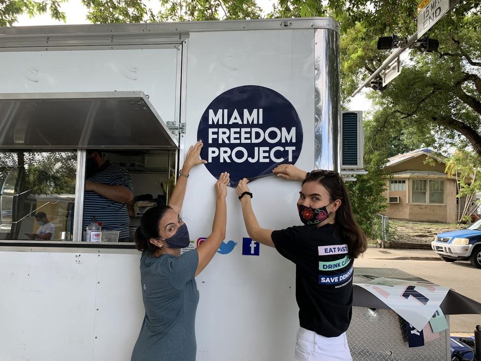 Two women putting up a sign that says "Miami Freedom Project".