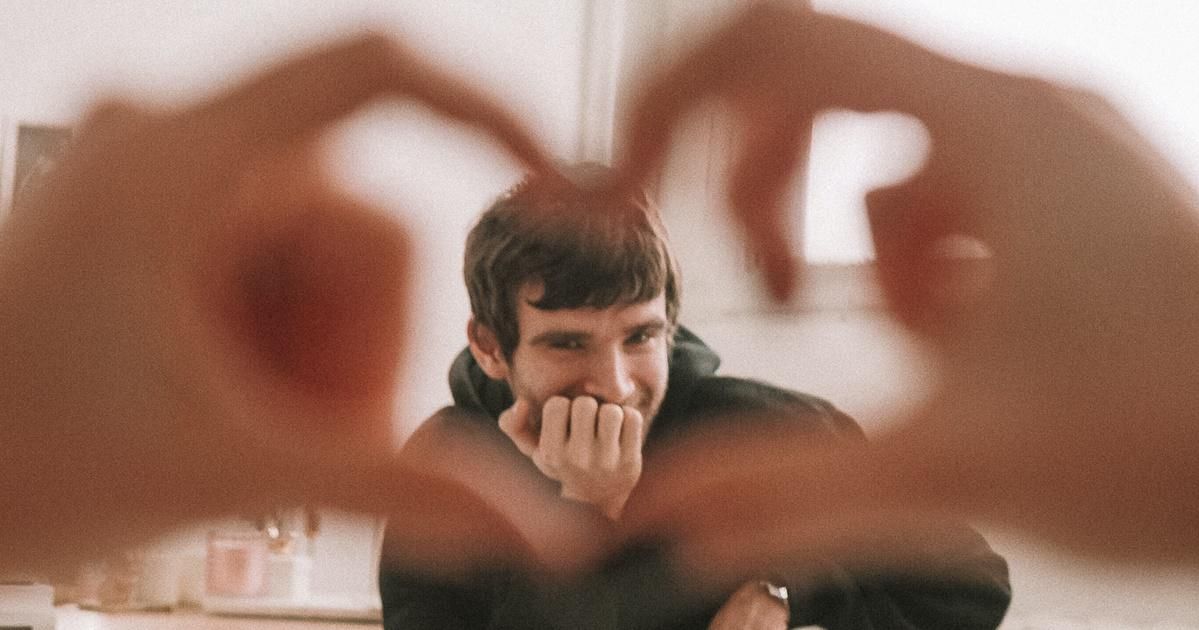 Man smiling behind heart hands
