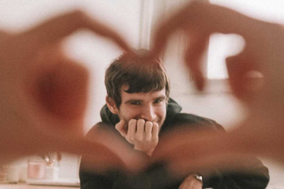 Man smiling behind heart hands