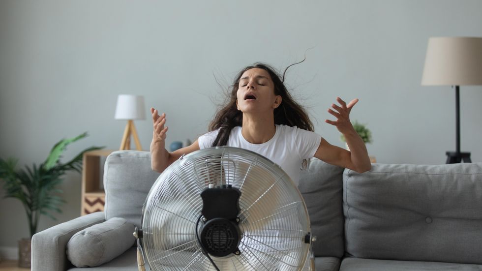 Woman sits on couch in front of fan