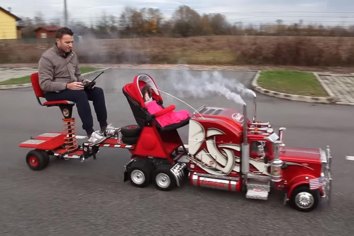 Screenshot of a large radio-controlled semi truck towing a small trailer holding the man who built it, and a baby carrier with a baby in it.