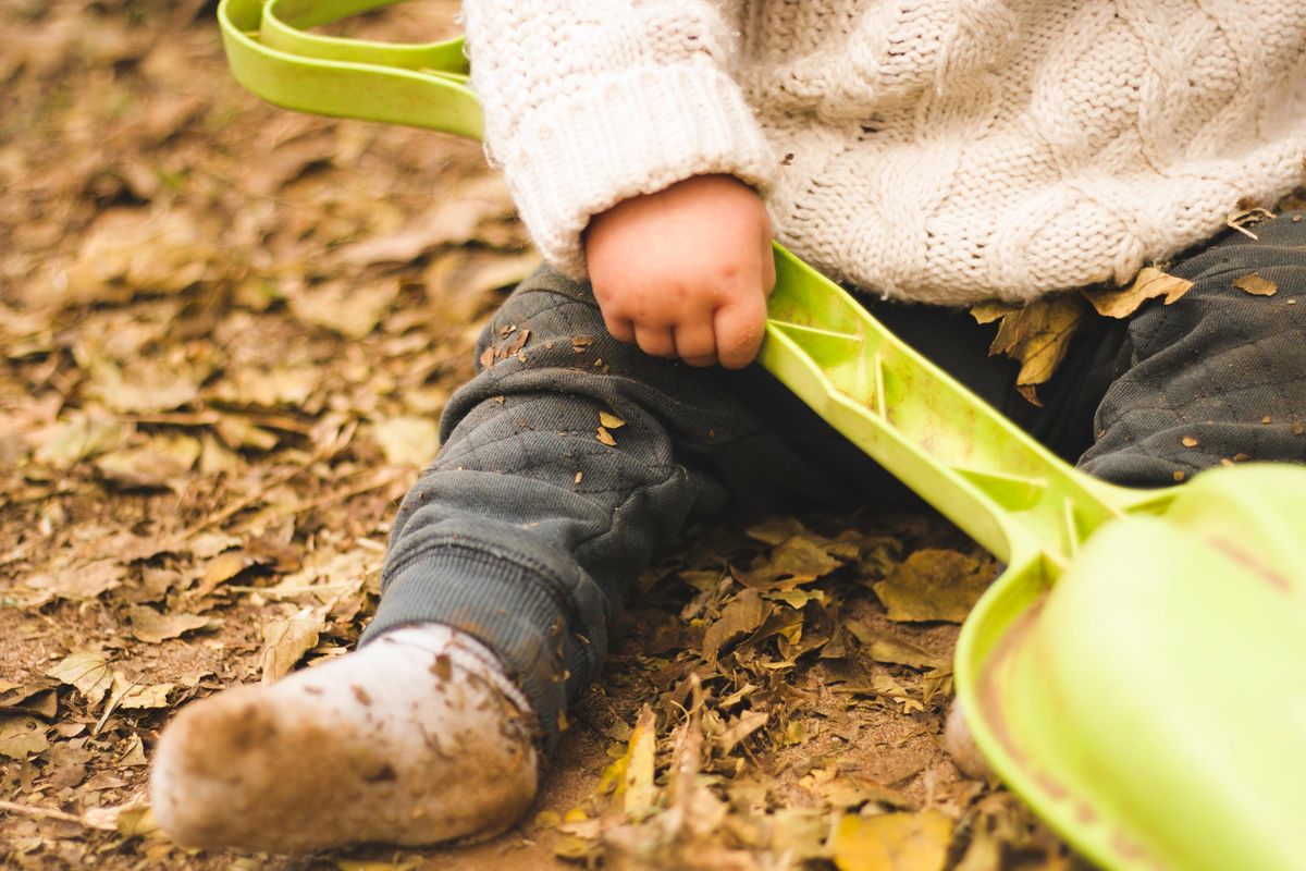 Close up of a toddler sitting in leaves playing with a toy