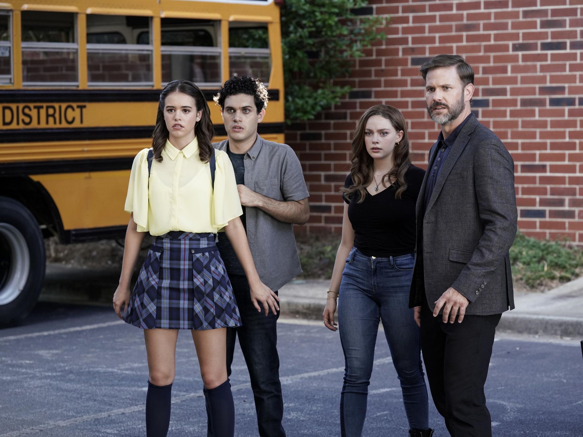 Josie, Landon, Hope, and Alaric stand next to a school bus in a parking lot looking warily into the distance.