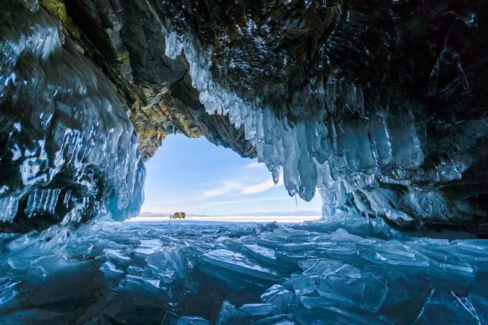 A photograph ⁤taken inside an ice ⁣cave‍ on Lake Baikal ⁤in⁤ Russia, showing a unique perspective with a car and people partially visible in the distance.