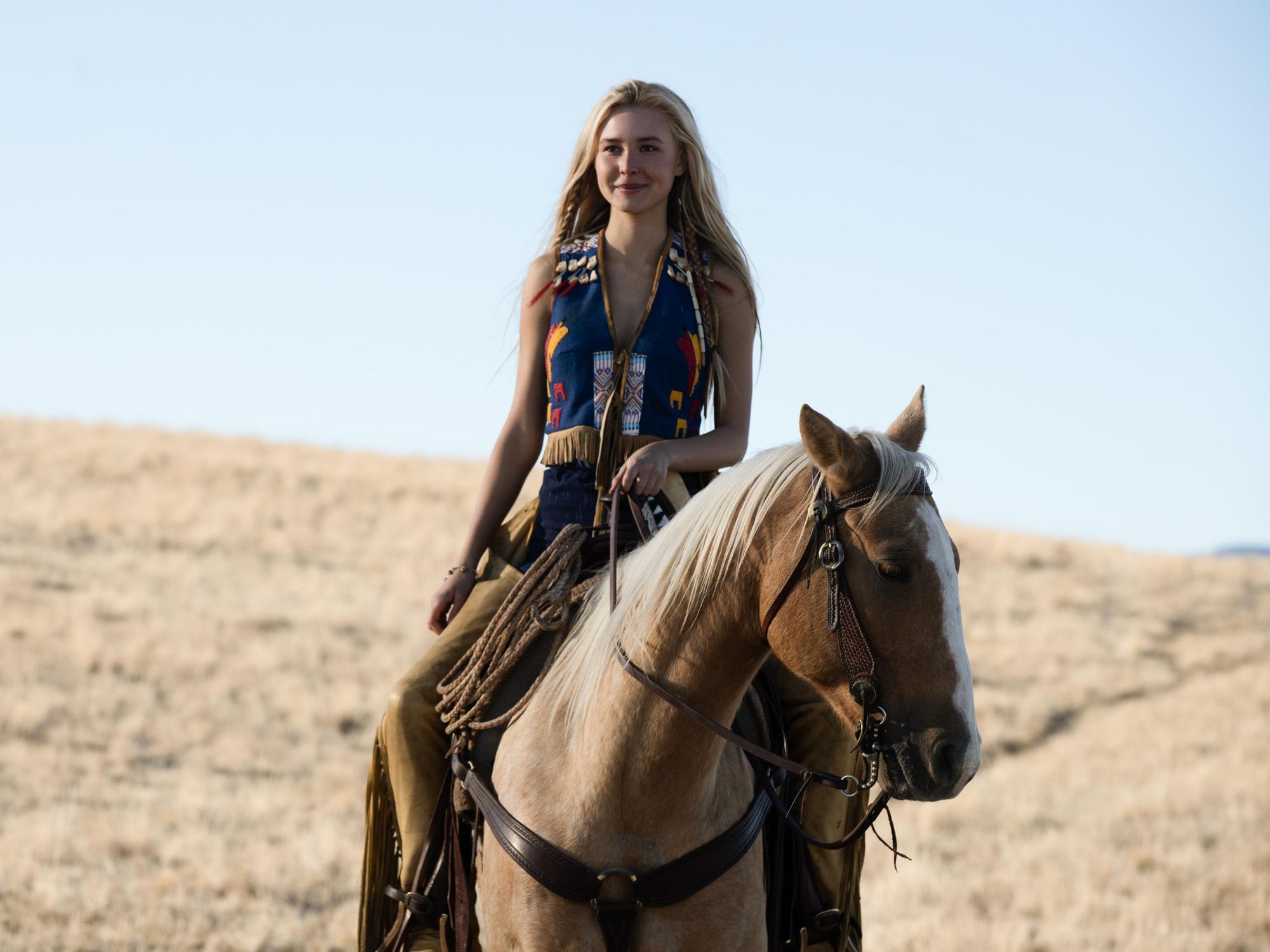 Isabel May as Elsa Dutton on horseback wearing yellow fringed chaps and a beaded blue, red, and yellow vest made for her by the Comanche
