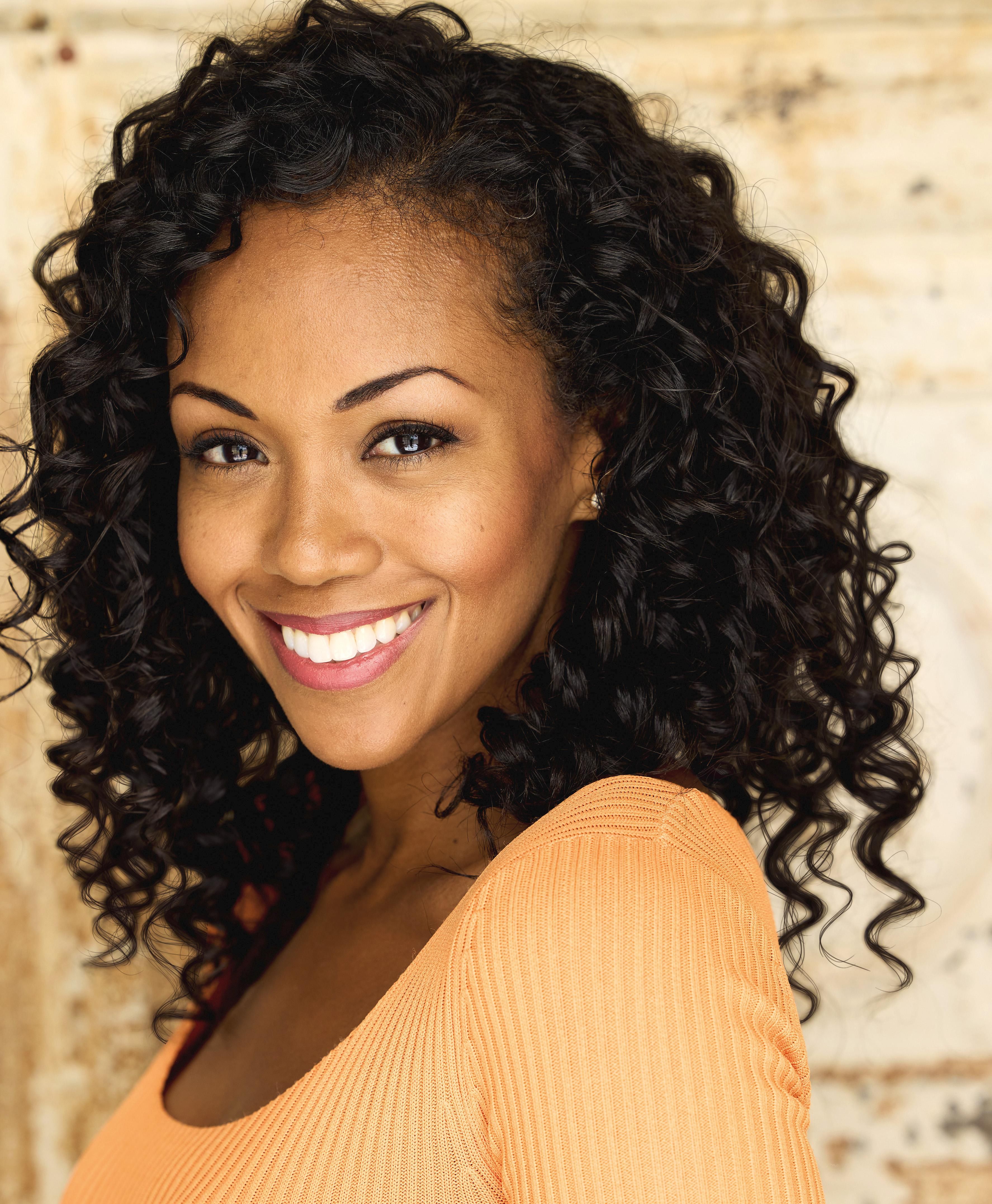 The Young and the Restless star Mishael Morgan wears a peach colored knit top while smiling broadly