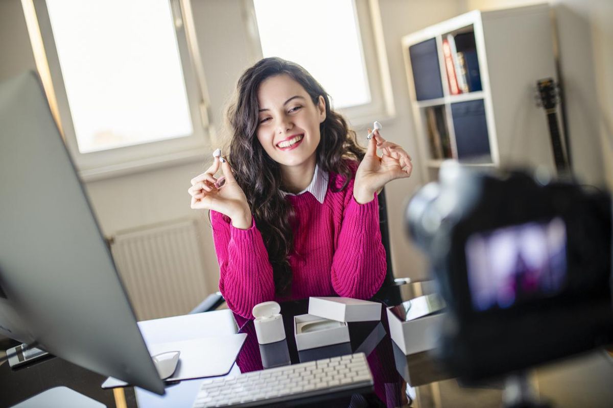 A photo of a woman doing an unboxing video for earbuds.