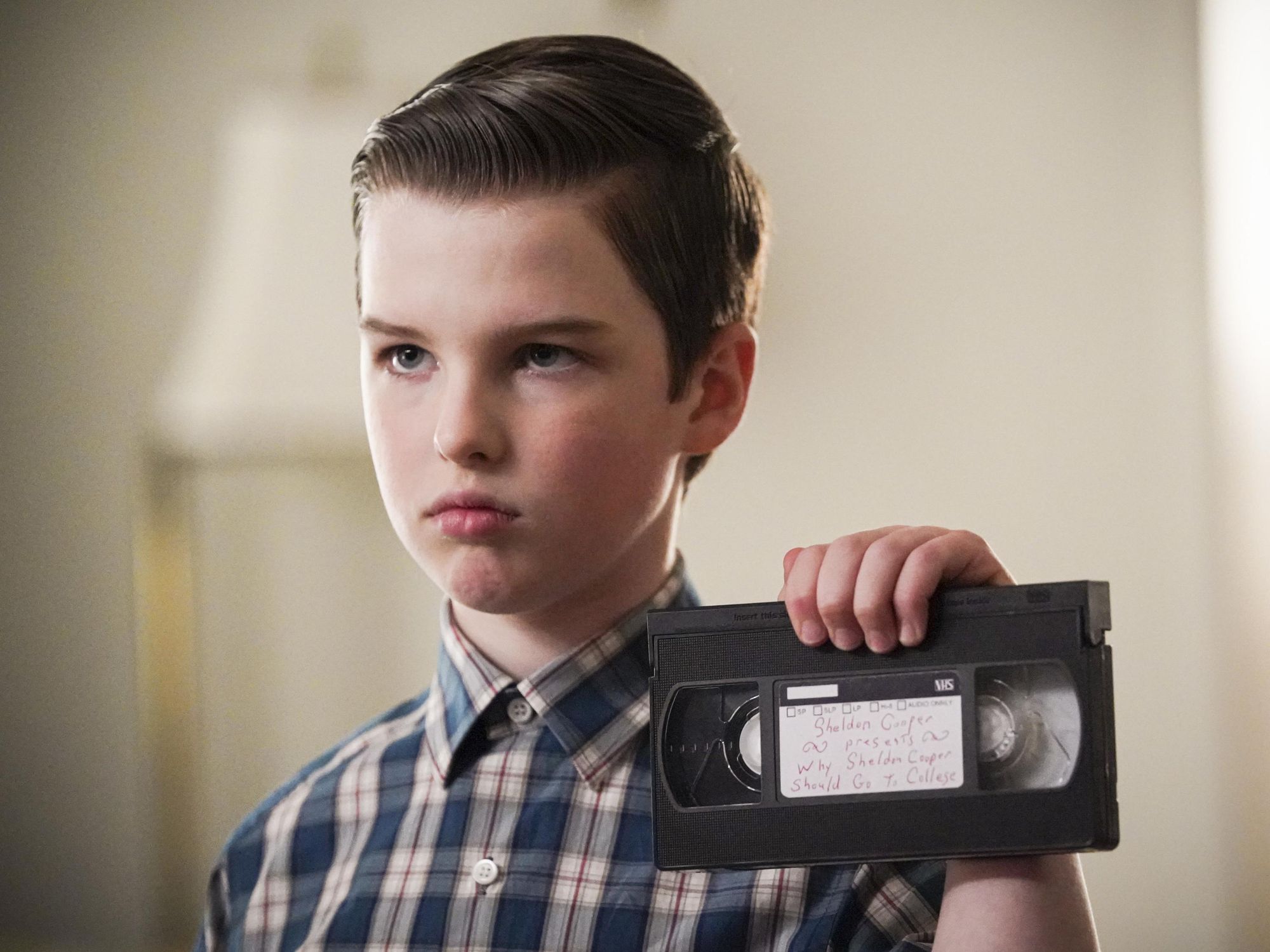 Young Sheldon looks stoic as he holds up a labeled videotape.