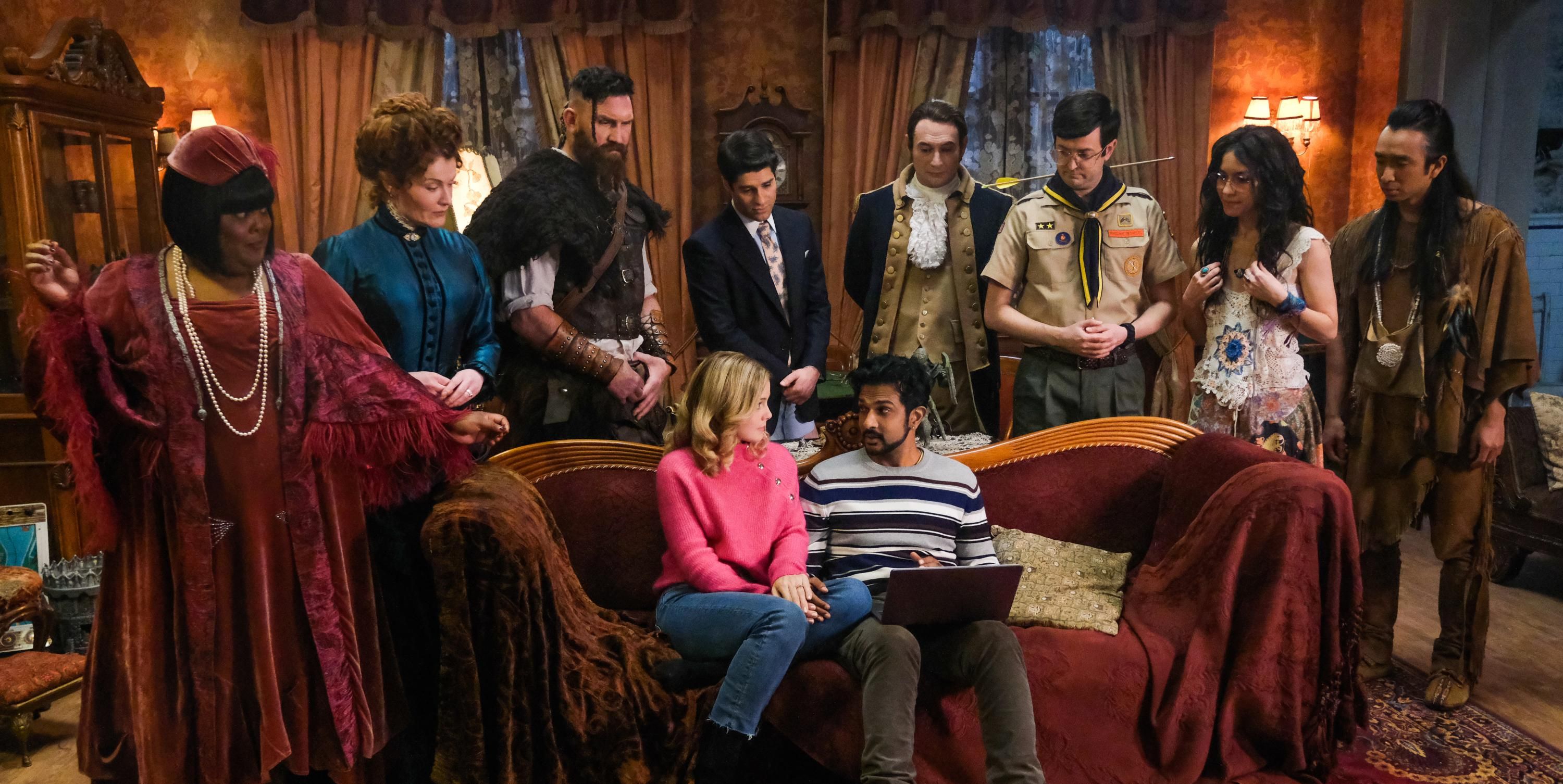 The entire cast of Ghosts on set gathered around a computer.