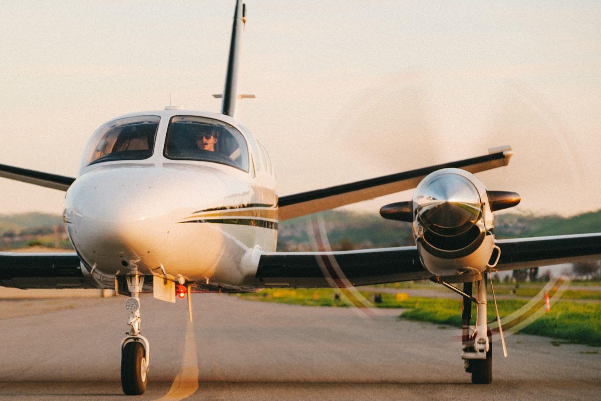 small white plane with black and gold stripes sitting on runway; propellers spinning