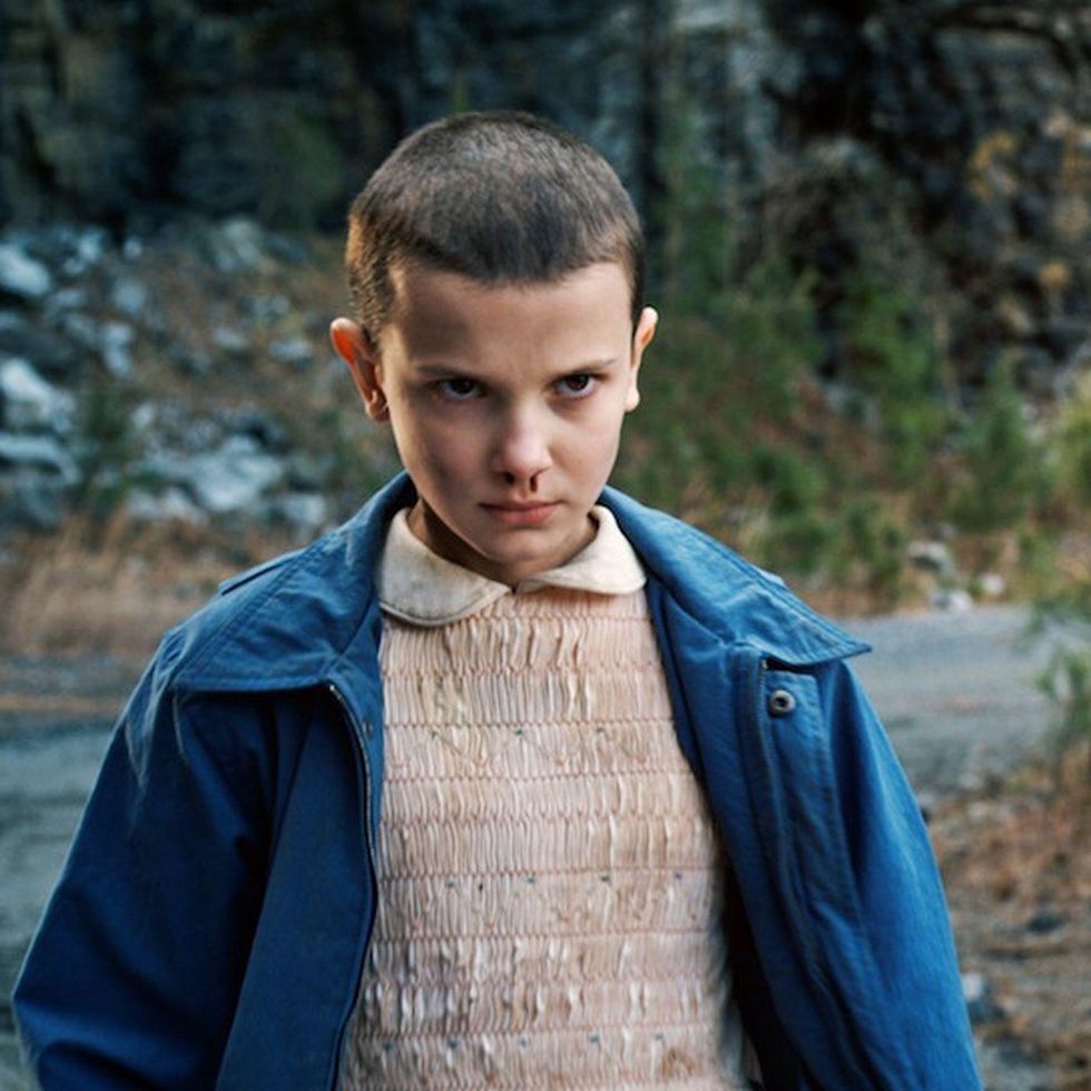 Eleven from Stranger Things Season 1 - short-haired girl in a pink dress with a nosebleed and intense stare