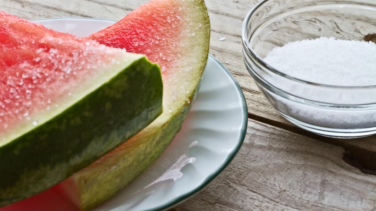 Slice on watermelon on plate to the left, bowl of salt on the right