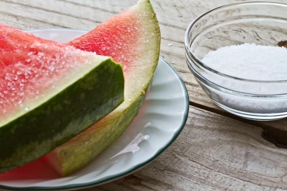 Slice on watermelon on plate to the left, bowl of salt on the right