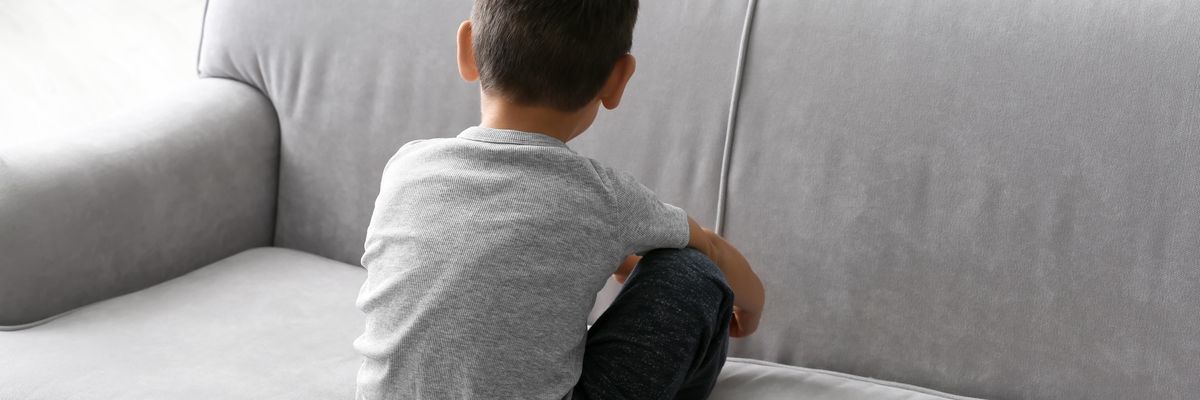 Boy sitting in a grey couch, giving his back to the camera