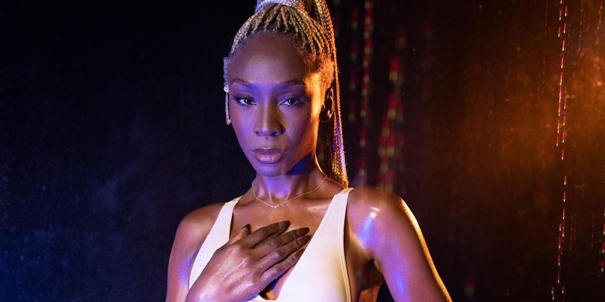 Angelica Ross, Black woman stands looking at the camera wearing a low-cut, cut-out dress, exposing her stomach. Her hand is over her heart