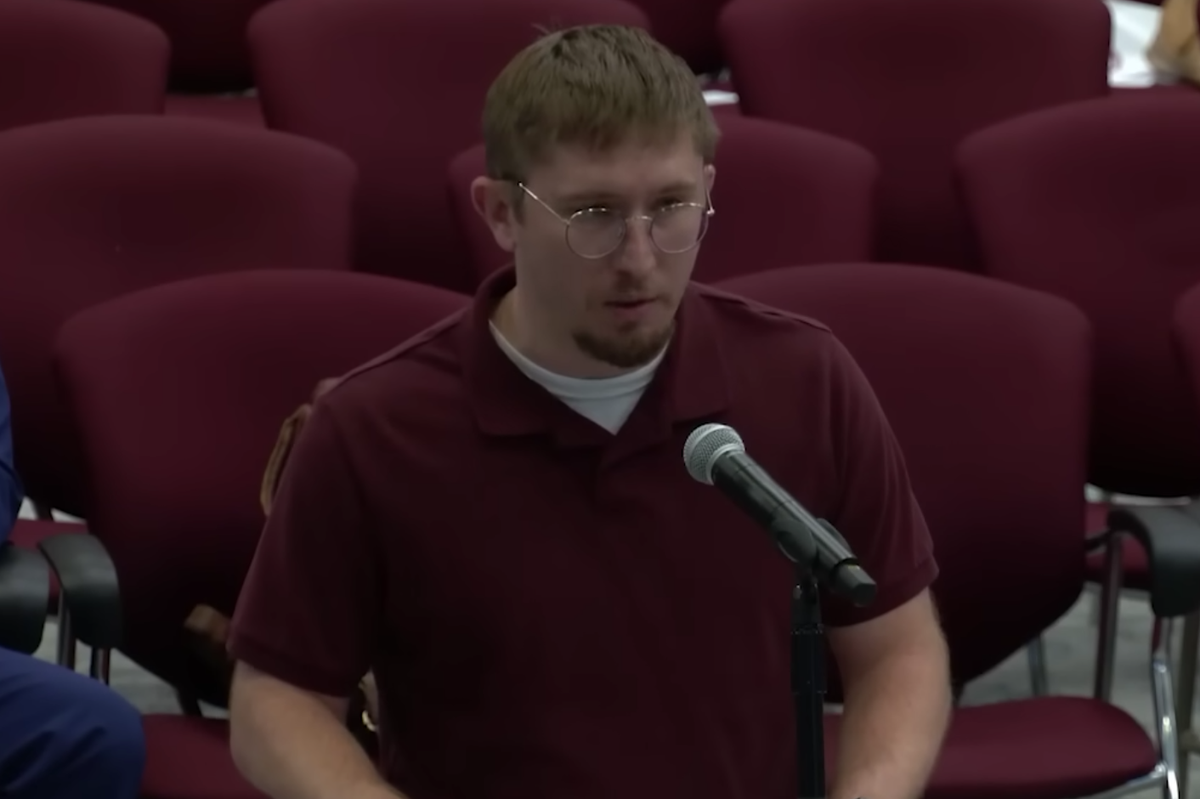 Man in maroon shirt speaking into a microphone at a public meeting.