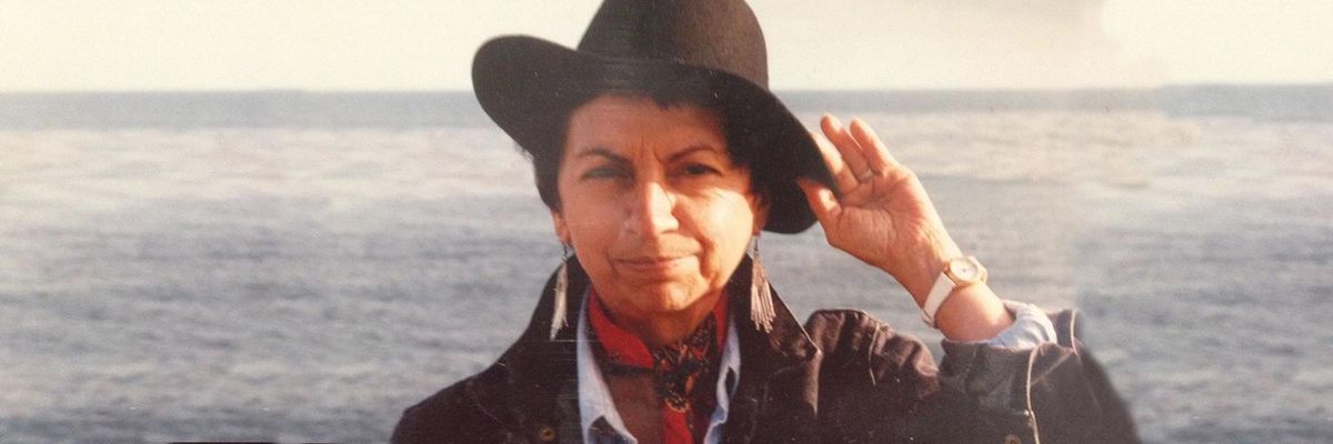 a photograph of Gloria Anzaldúa with a hat with the sea behind her
