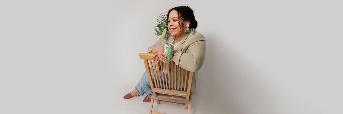 woman sits on chair looking away from the camera with a canned beverage in her hand