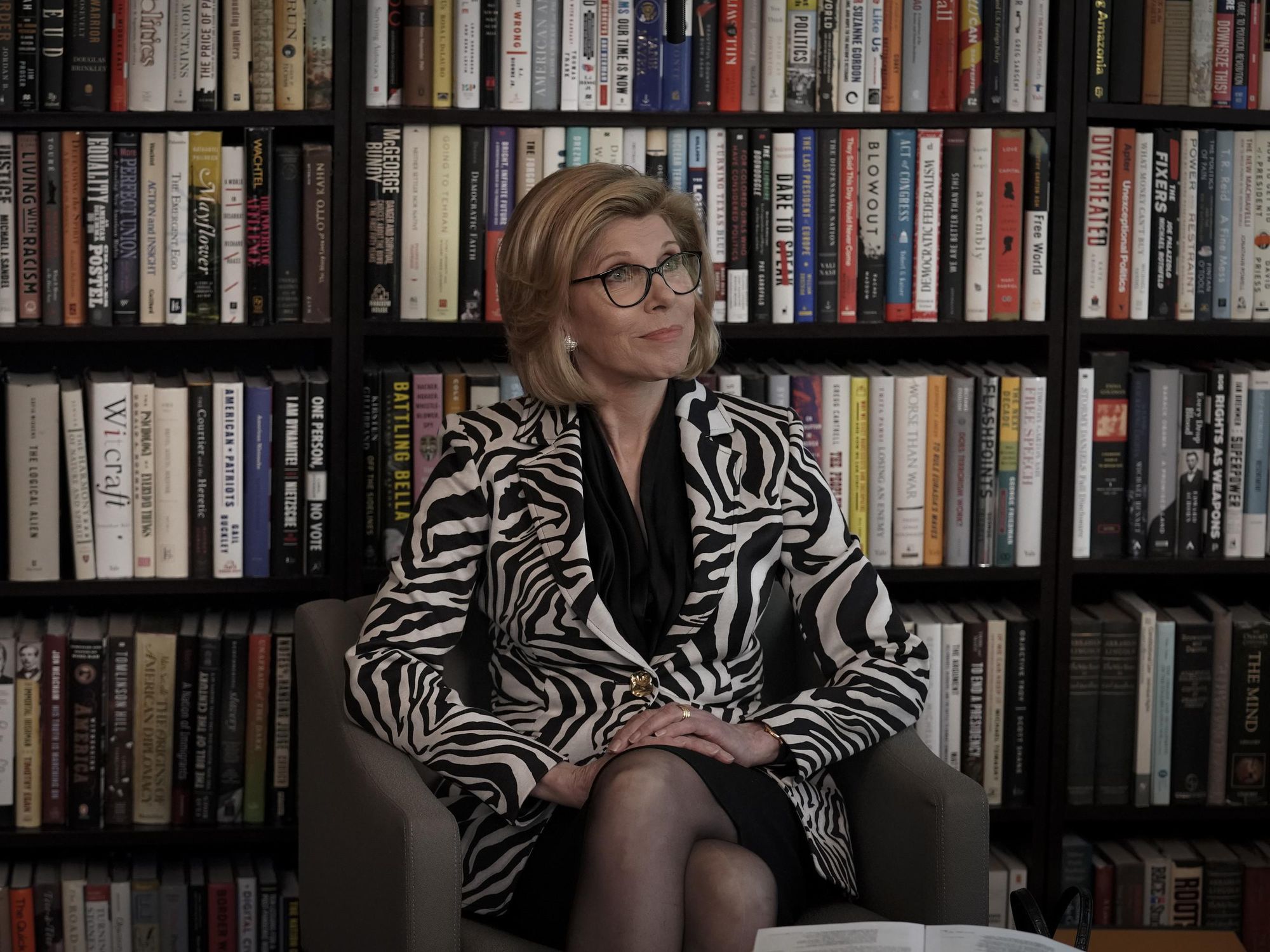 Diane Lockhart sitting wearing a zebra print jacket in front of a wall of books