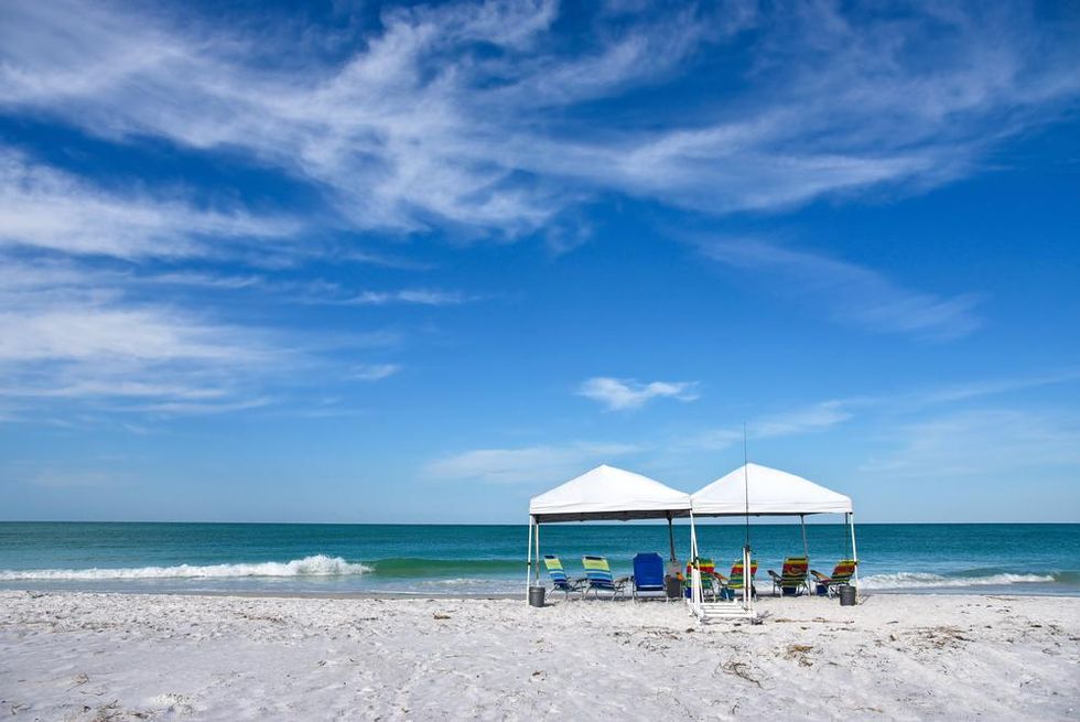 Two tents with beach chairs underneath set up on sand