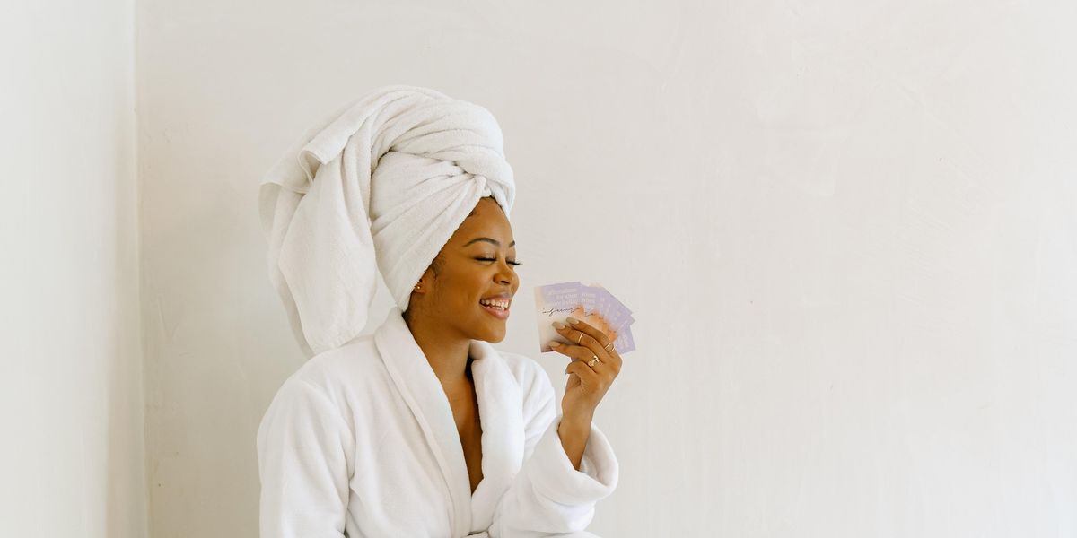 A Black woman in a white bathrobe with a white towel wrapped around her head smiles