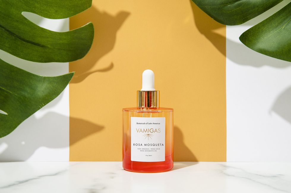 Beauty product liquid vial sitting on a marble countertop in front of plant leaves and a yellow background