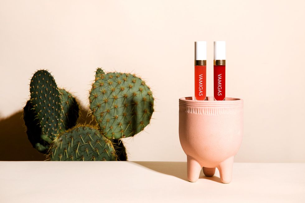 Image of two lip oils on a ceramic planter on a white table in front of a cactus plant