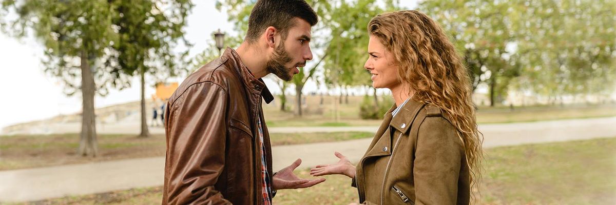 Man and woman arguing in an open space with trees in background