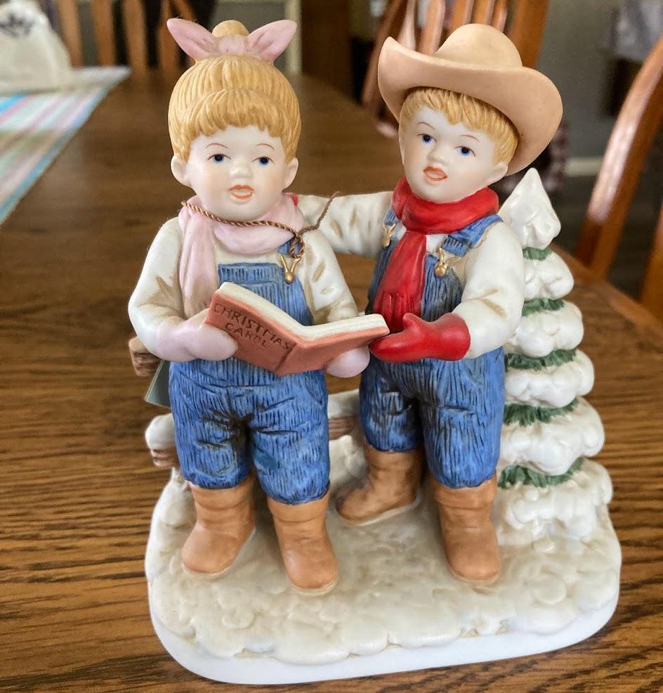 Denim Days figurine of boy and girl holding Christmas carol book and singing in front of snowy trees