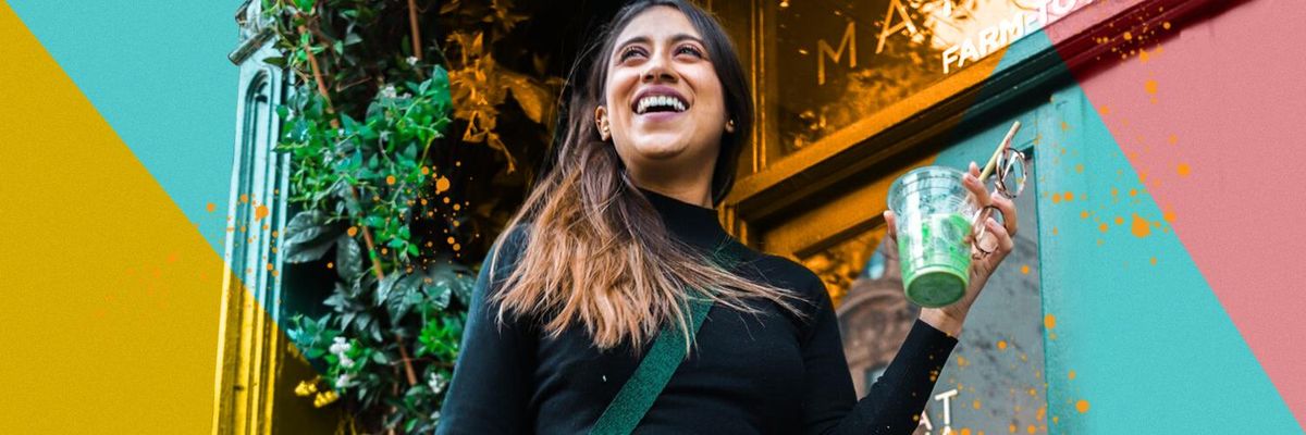 Imagine of a woman smiling while holding an iced drink and glasses in front of a colorful background