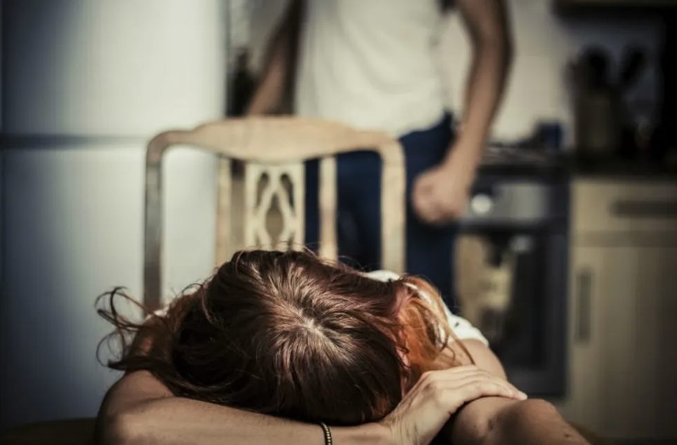 woman with her head down on a table while man with clenched fists stands behind her.