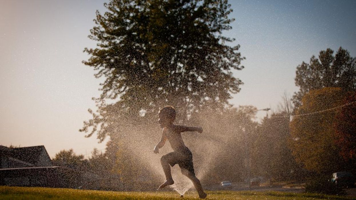Silhouette of child playing in sprinkler on lawn