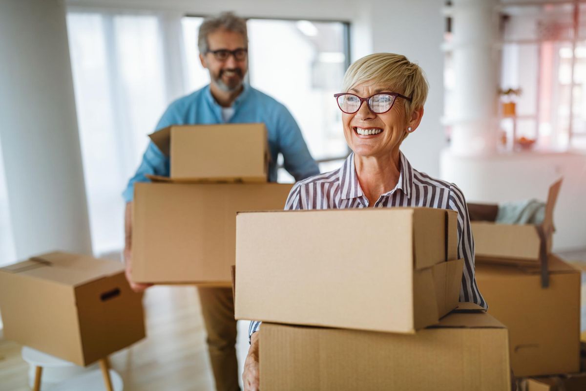 A happy senior couple holds moving boxes.