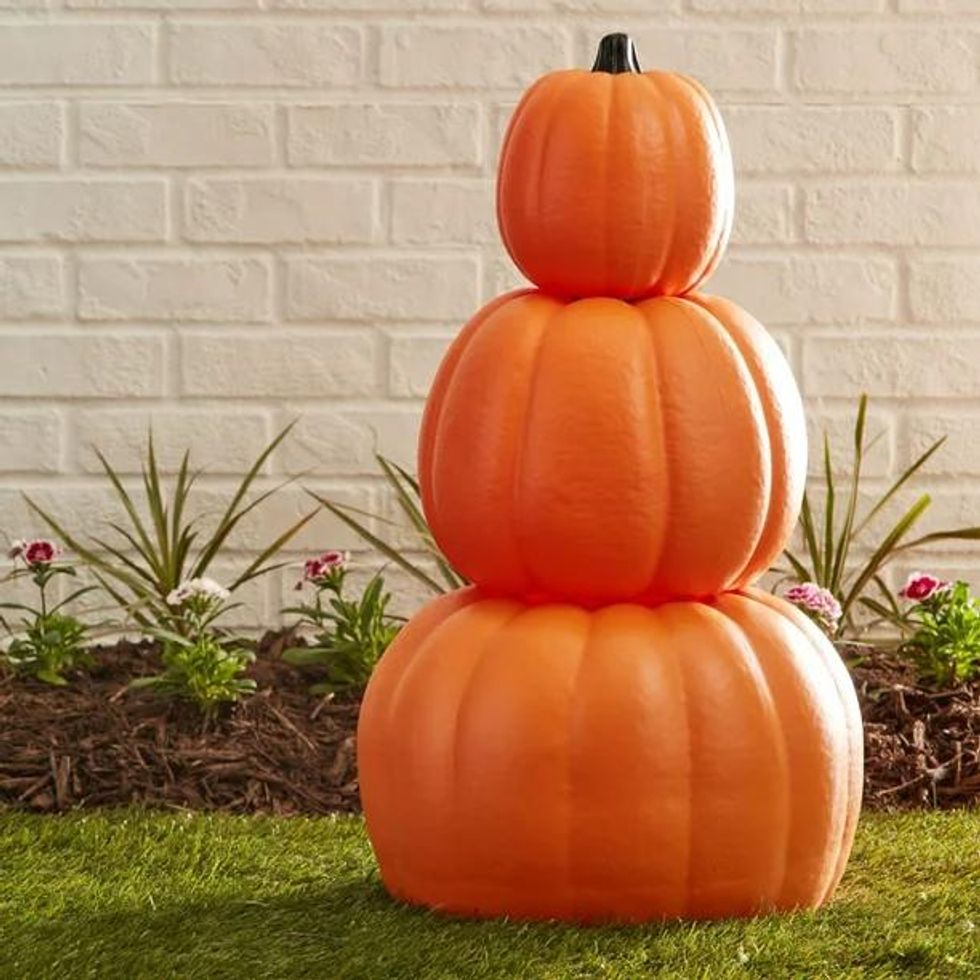 Three stacked pumpkins sit on a green lawn.