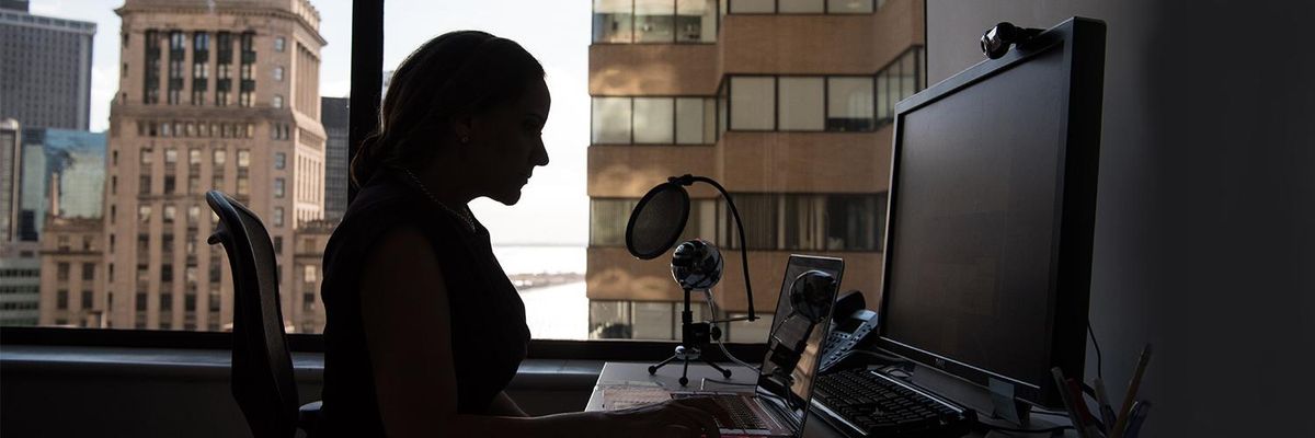 Side profile of a woman sitting at a desk looking at her laptop in front of a city skyline