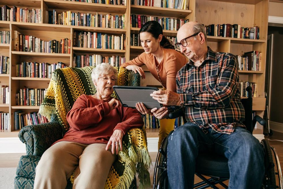 a photo of elderly couple with a caregiver looking at a tablet