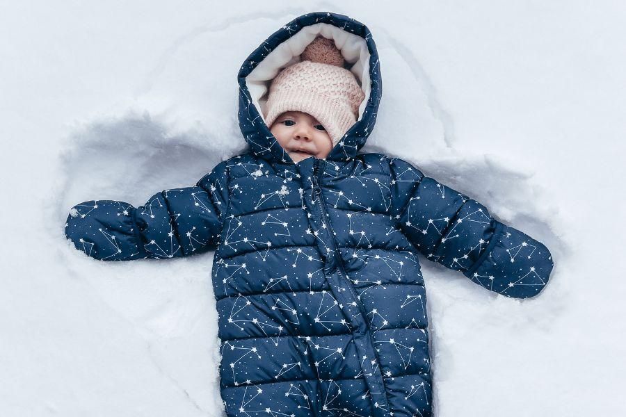 Baby in blue snowsuit lying in the snow